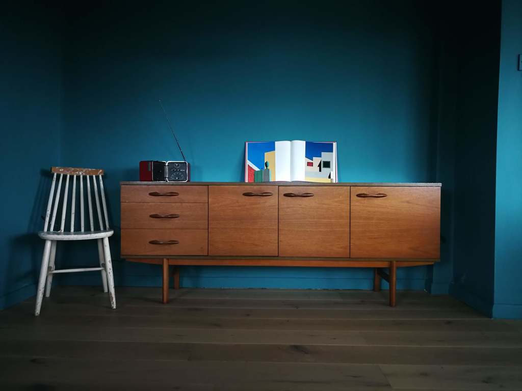 Mid century modern sideboard styled with vintage FM radio and artbook and reclaimed wooden chair. Walls and trim in the same teal paint