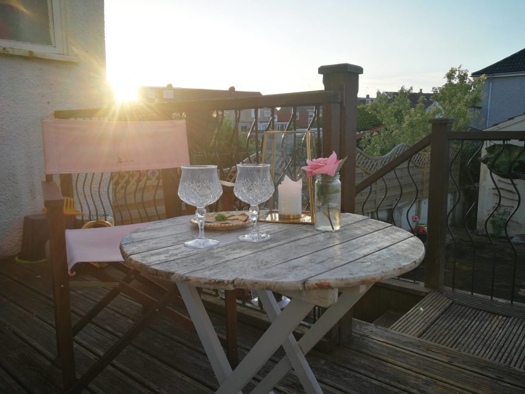 An upcycled coffee table on a patio overlooking a garden. Two Murano glasses, a candle and a glass jar with a fresh rose, suggest an informal, relaxed atmosphere.