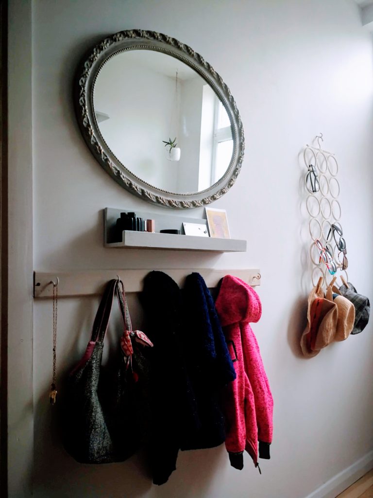 Children coat hanger in the hallway. Above the coat hangere there is a vanity shelf with essential make-up and an upcycled mirror painted in french grey. An Ikea white multi-use KOMPLEMENT hanger to hold sunglasses and sun hats