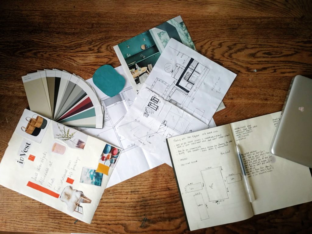 Selection of materials suggesting craftsmanship in interior design. A notebook with handwriting, sketches for a bathroom design, a colour card, a mood board with inspirational pictures.