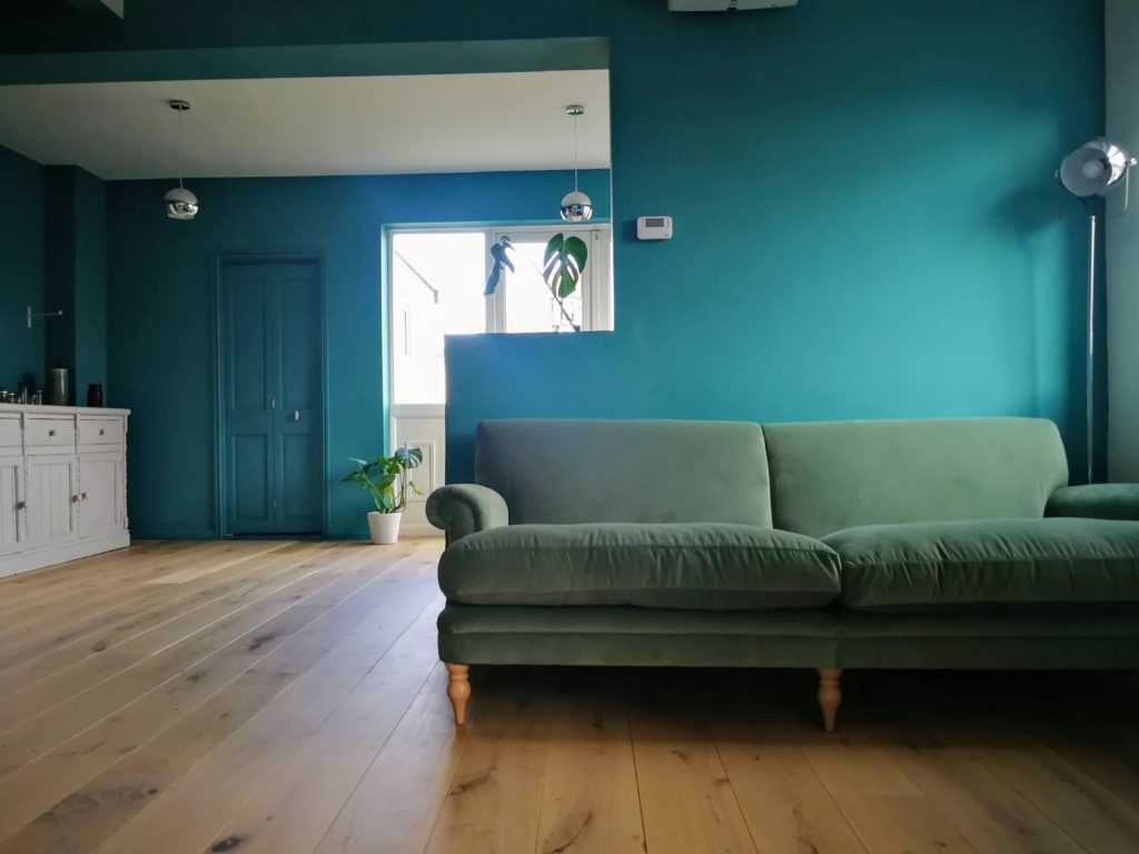 Contemporay, minimalist semi open plan living room and kitchen with engeneered wood and teal walls. Green velvet Agatha sofa by Arlo and Jacob
colour scheme for living room with green velvet sofa, walls and trim painted the same colour