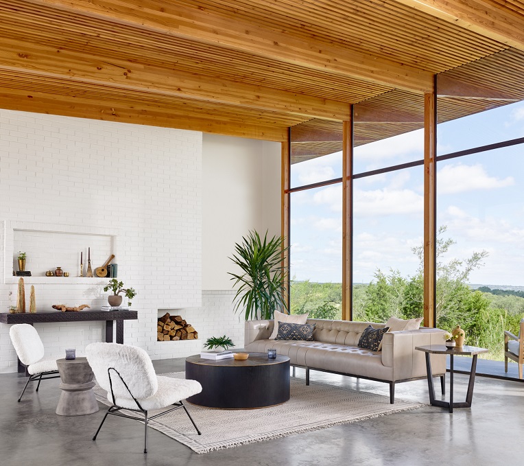 stunning contemporary and warm living room with full-length glass walls and cement floor. Example of a typical feng shui living room impacting the inhabitant's well-being. The whitewashed brick wall, the cement flooring and the squared design of the sofa call for a contemporary style. The wooden slat sculptural ceiling adds warmth to the scheme and a feel of Japanese style. The room is complemented with two accent chairs in white sheepskin fabric and a black round wood coffee table. Overall it conveys a sense of calm and happiness and connection to nature
