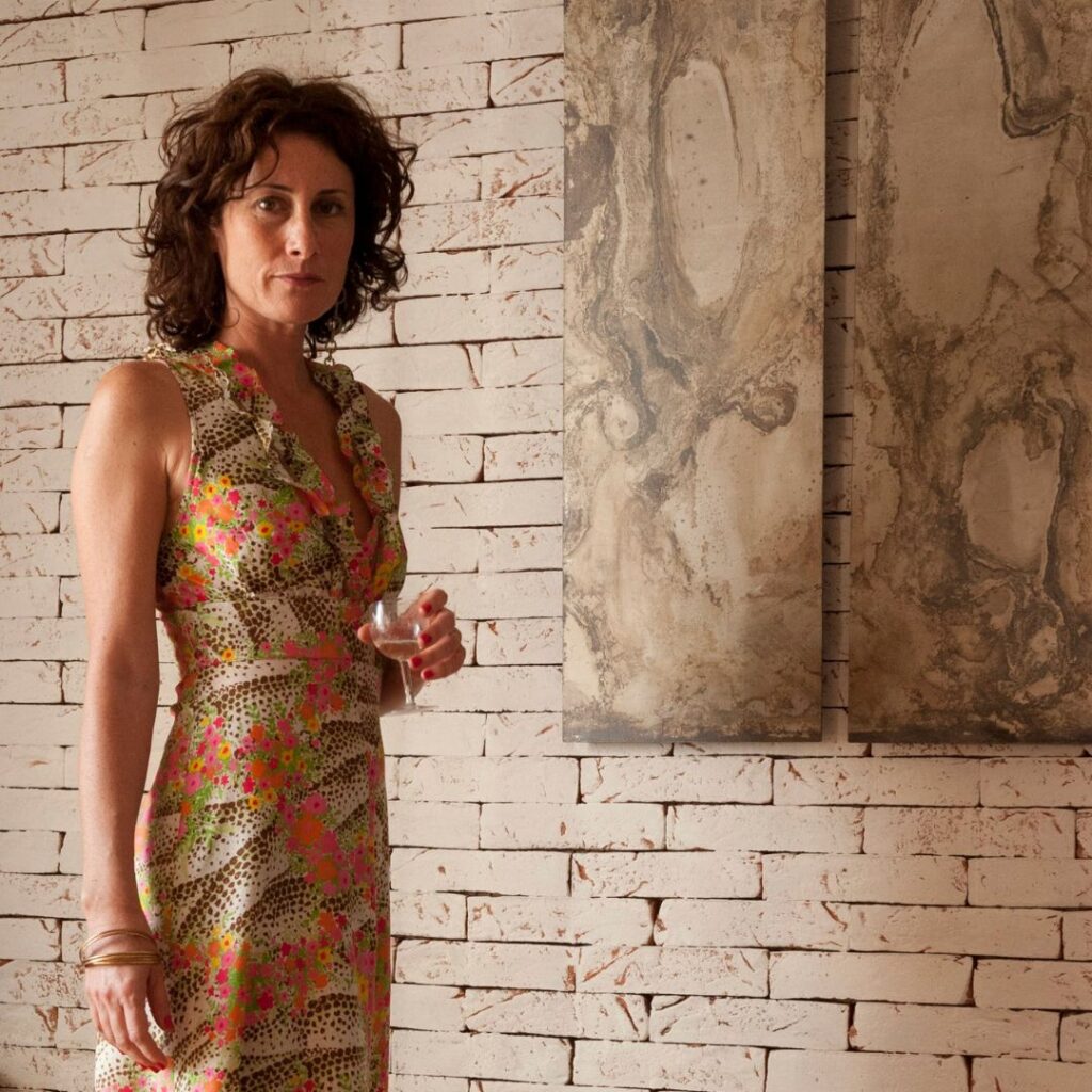Marta Rossato wearing a colourful silk dress on a white-washed brick background wall. Artwork from Monica di Brigida