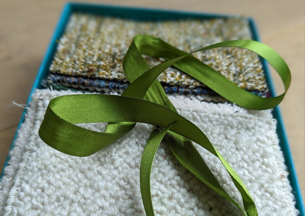 Teal card paper box with a selection of tactile upholstery fabrics and a green silk ribbon