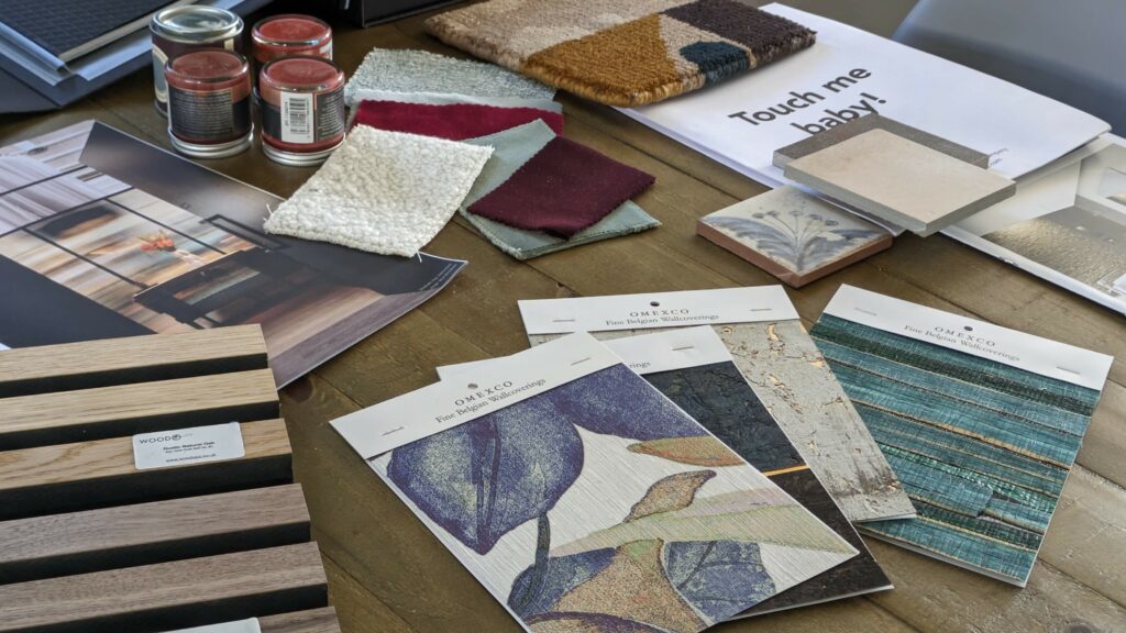Design presentation including beautiful samples of floral wallpaper, tactile fabrics, wool rug, wooden panels and paint pots and tiles.